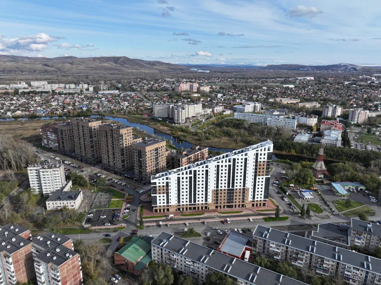 Панорамный вид с воздуха на город с новым белым и черным жилым зданием, расположенном у реки и окружённым другими домами.